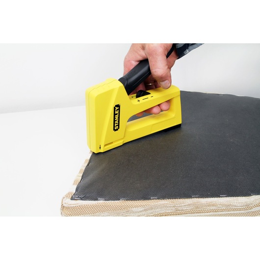 STANLEY STHT6-70409 yellow staple gun used for upholstery on a gray cushion, close-up.