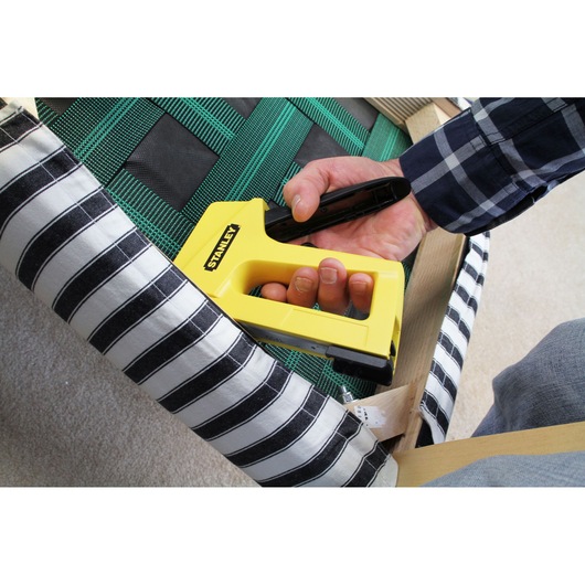 STANLEY STHT6-70409 stapler being used on striped upholstery, close-up photography.