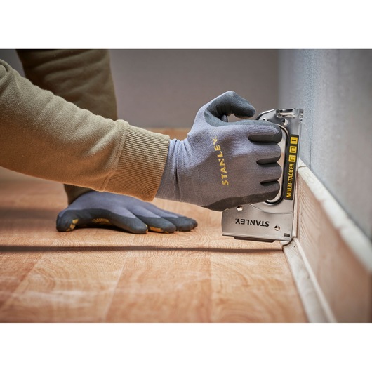 STANLEY STHT6-70410 multi-tacker used on floor trim, close-up angle, gloves visible.