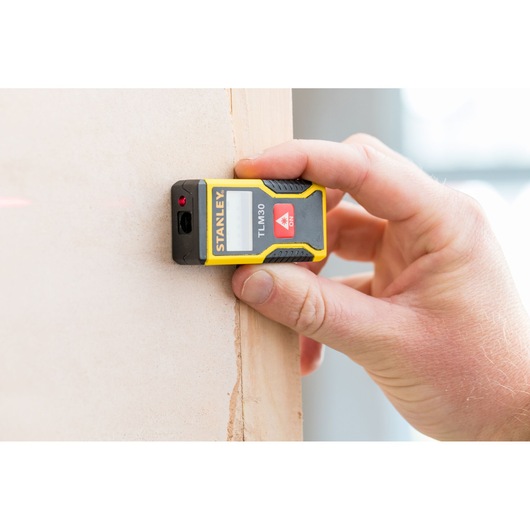 Photo of STANLEY STHT9-77425 laser distance measurer held against a wall, showing yellow and black design.