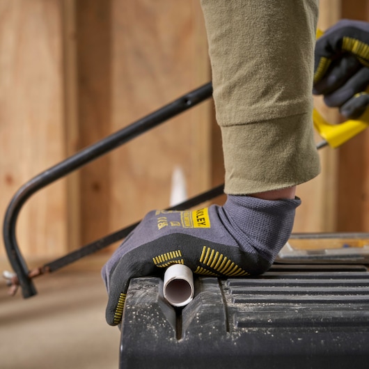 STANLEY STST1-70715 work glove holding pipe on toolbox during sawing, close-up.