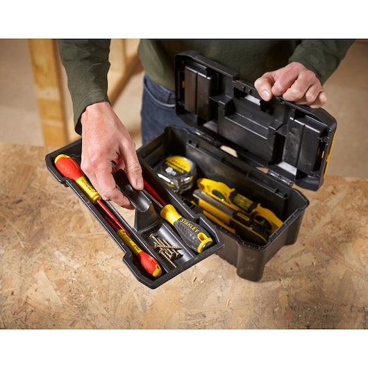 STANLEY STST1-75515 black toolbox photography, open top view with hand holding removable tray and assorted tools inside.