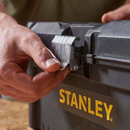 STANLEY STST1-75518-KR toolbox close-up, hand opening metal latch, black case, yellow logo.