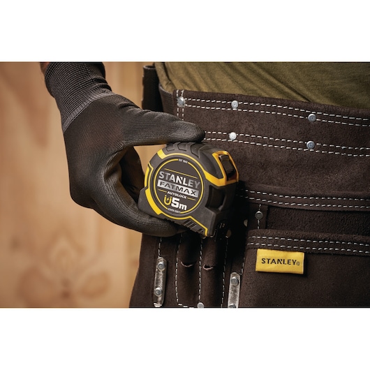 STANLEY XTHT0-33671 tape measure held in hand, yellow and black casing, extended measuring blade, close-up front view.